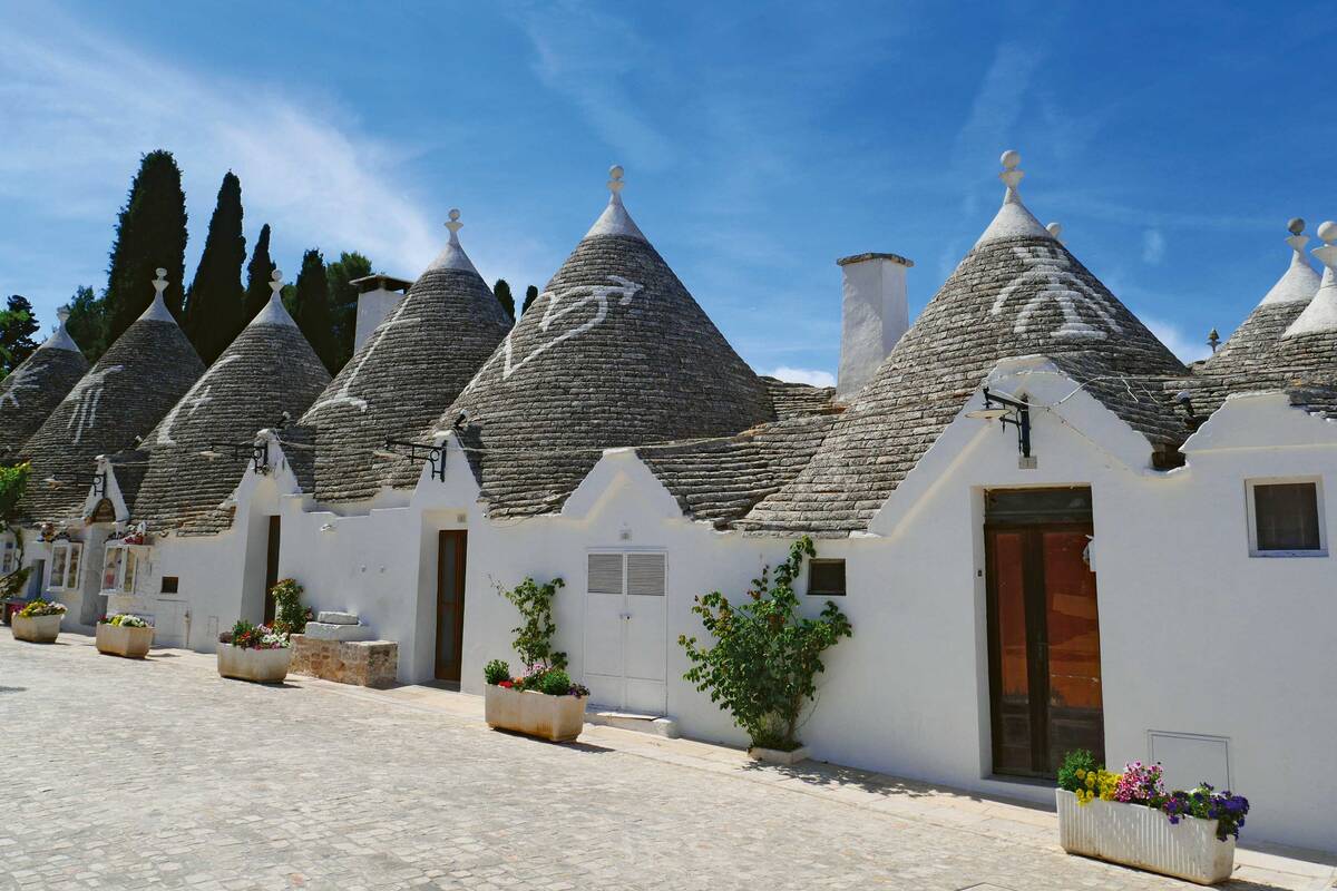Trulli in Alberobello mit kugelförmigen Dachspitzen und schützenden Zeichen auf dem natursteinfarbenen Dach.